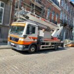 Camion monte-charge Delleuse Marc Toitures garé devant une maison sur une route en pavés