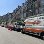 Camionnettes, monte-charge et echafaudage devant une maison mitoyenne dont la toiture doit être rénovée