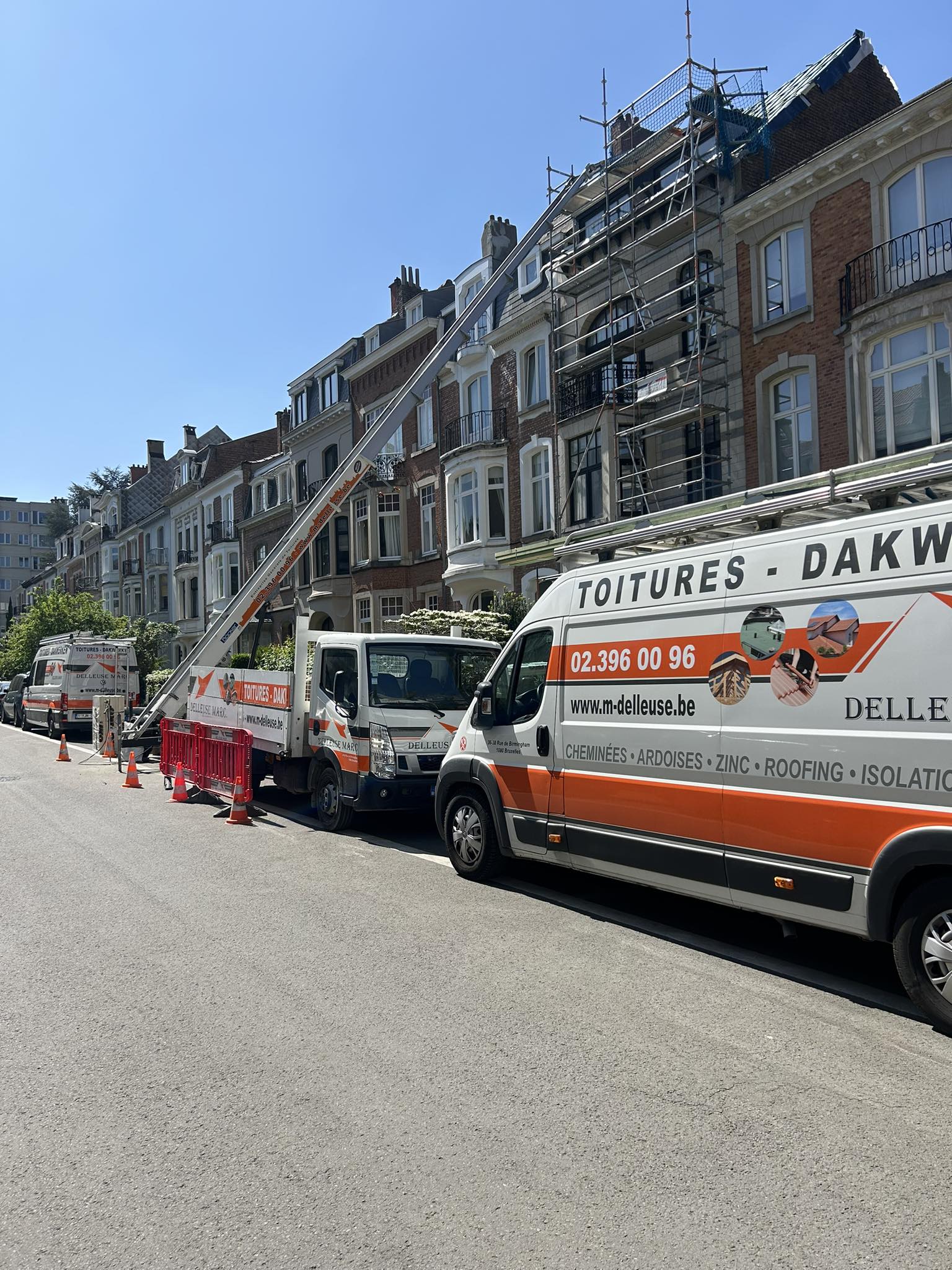 Camionnettes, monte-charge et echafaudage devant une maison mitoyenne dont la toiture doit être rénovée